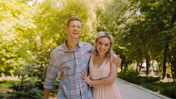 Девушка искренне улыбается, счастливая пара гуляет в летнем парке, романтическое свидание
