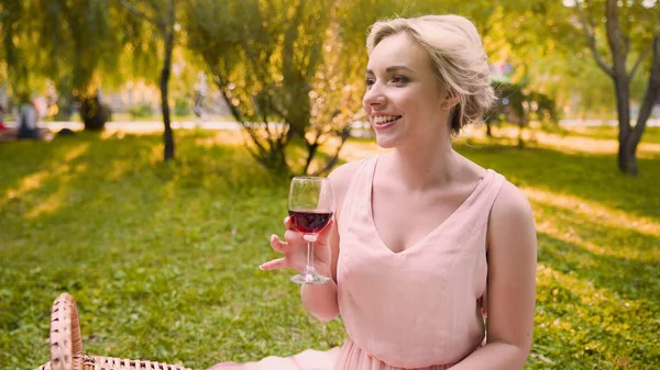 Красивая девушка, потягивающая вино в тени деревьев парка, прекрасно проводит время в парке — стоковое фото