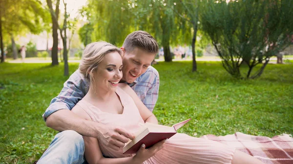 Chico leyendo libro a su novia, pareja disfrutando de ocio en parque juntos — Foto de Stock