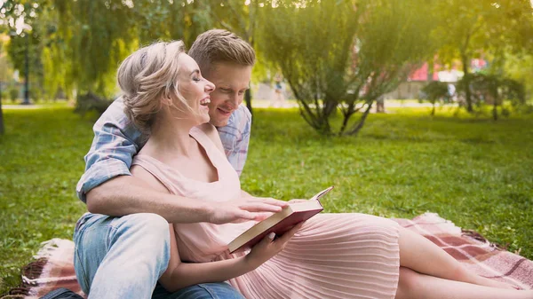 Веселая пара, наслаждающаяся отдыхом в парке, читая книгу и веселясь вместе — стоковое фото