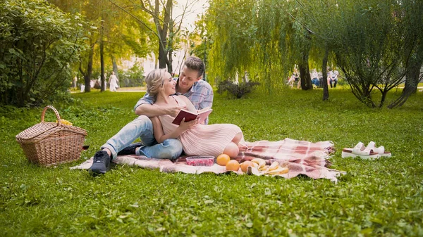 Tierna pareja discutiendo libro, sentado en la alfombra durante el picnic, cita romántica — Foto de Stock