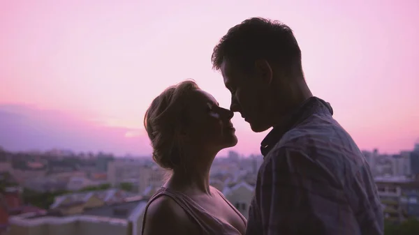 Amantes bonitos gentilmente abraçando, de pé no telhado, belo pôr do sol fundo da cidade — Fotografia de Stock