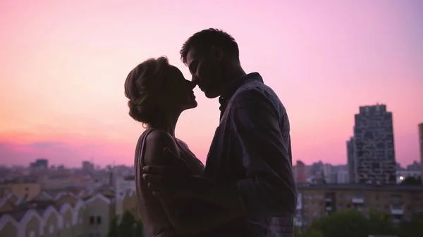 Par i kärlek varsamt kysser, stående på taket av huset, vacker solnedgång — Stockfoto