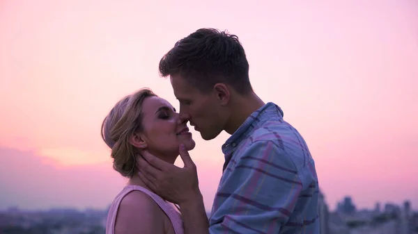 Loving couple passionately kissing, meeting dawn on roof of high-rise building