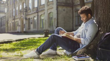 Park, ağacın altında oturan karışık ırk adam okuma kitabı, boş zaman, hobi