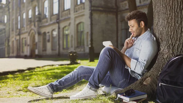Multiracial joven sentado con cuaderno bajo el árbol, pensando qué escribir —  Fotos de Stock