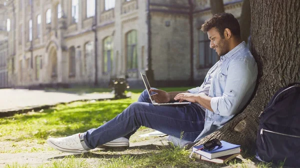 İyi haber, duygular gülümseyen ağaç altında laptop kullanarak genç karışık ırk adam