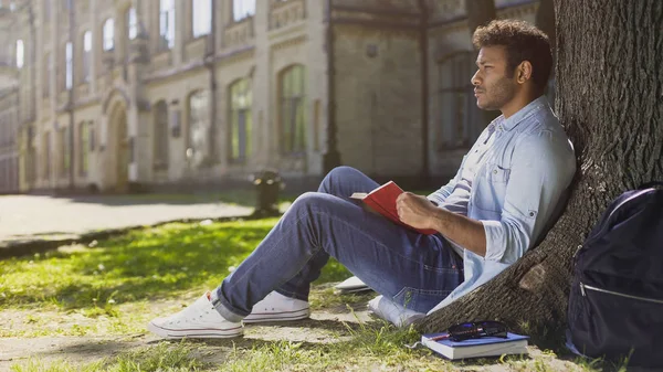 Estudante universitário do sexo masculino sentado sob árvore, livro de leitura, memorizando informações — Fotografia de Stock