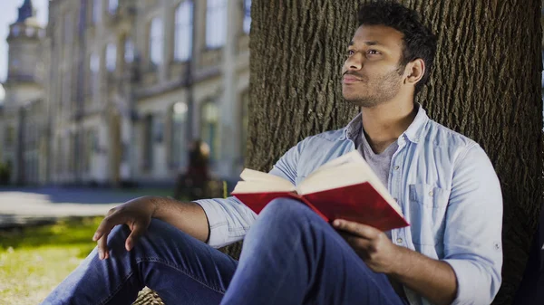 Mladý muž, sedící pod stromem čtení knih a myšlení, odborné literatury — Stock fotografie