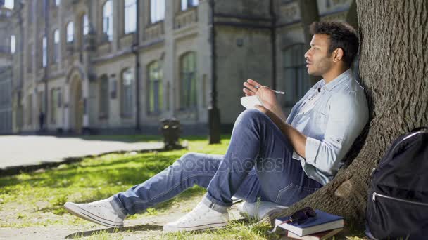 Mixed-race young guy sitting under tree, taking notes in notebook, inspiration — Stock Video