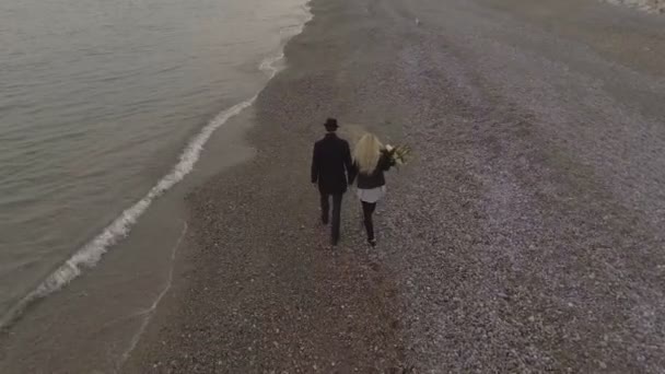 Dating couple walking on seashore holding hands, girl carrying flowers, date — Stock Video