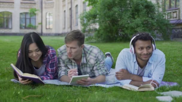 Companheiros de raça mista descansando no gramado no campus universitário, desfrutando de hobbies — Vídeo de Stock