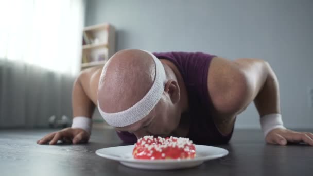 Uomo grassoccio sdraiato sul pavimento, che si rifiuta di mangiare appetitosa ciambella dolce, perdita di peso — Video Stock