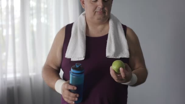 Korpulenter Mann trinkt stilles Wasser und isst grünen Apfel nach dem Training, Diät — Stockvideo