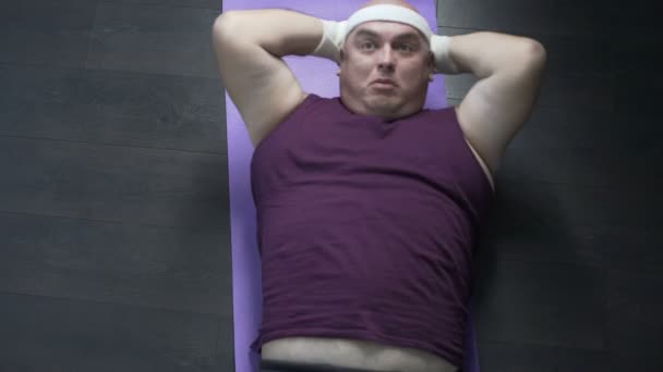 Смешной человек с избыточным весом делает хрусты с большим усилием на мат, теряя вес — стоковое видео