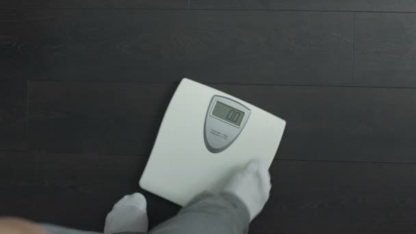 Vue du dessus de l'homme gras marchant sur des échelles de santé et regardant l'affichage, l'obésité — Video