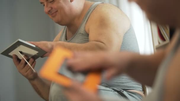Obézní muž, sedící v přední části zrcadlo a při pohledu na fotografii rodiny s láskou — Stock video