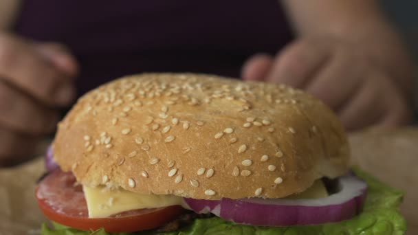 Muž ruce brát hamburger s rajčaty a cibulí z tabulky, přibývání na váze, makro — Stock video