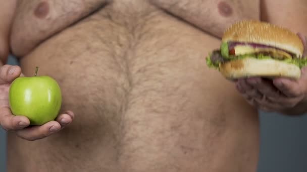 Gros homme hésite à choisir pomme ou hamburger, vitamines décision de santé — Video