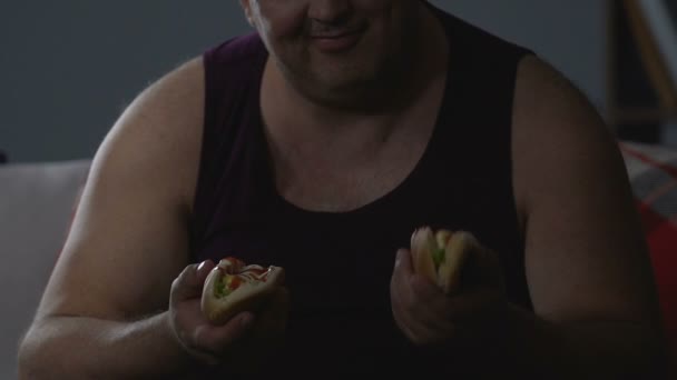 Голодные мужчины едят два хот-дога, нездоровая пищевая зависимость, психологические проблемы — стоковое видео