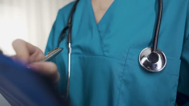 Young nurse writing down patient information into hospital form, emergency ward — Stock Video