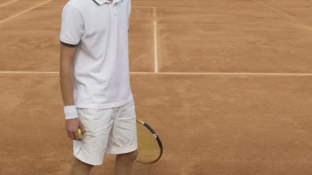 Male athlete in sportswear holding racket and tennis ball, training on court — Stock Video