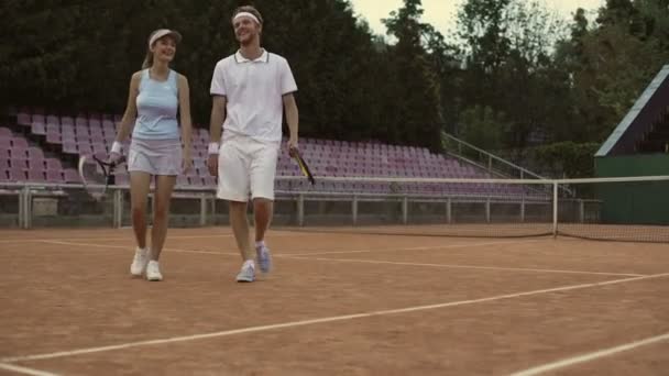 Uomo e donna in abbigliamento sportivo bianco che camminano sul campo, preparandosi a giocare a tennis — Video Stock