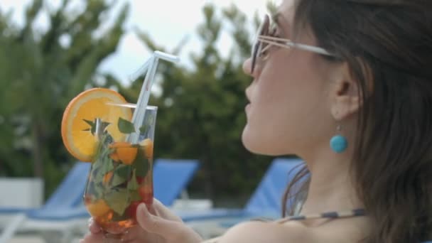 Chica disfrutando del sabor de cóctel fresco sentado junto a la piscina de su lujosa mansión — Vídeos de Stock