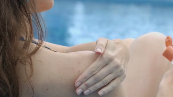Жінка ретельно наносить зволожуючий лосьйон на тіло відпочиваючи біля басейну — стокове відео