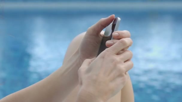 Mujer sentada junto al agua y escribiendo un mensaje en el teléfono inteligente, correspondencia en línea — Vídeo de stock