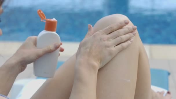 Леди наносит лосьон для загара на ноги с массажными движениями, отдыхающими у бассейна — стоковое видео