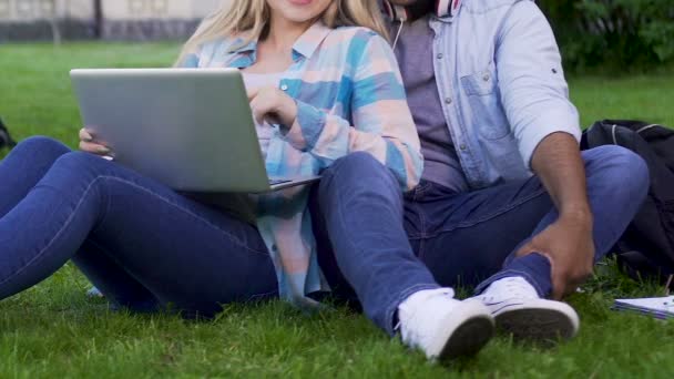 Dos jóvenes sentados en la hierba, chica apoyada en el chico y sosteniendo el ordenador portátil — Vídeo de stock