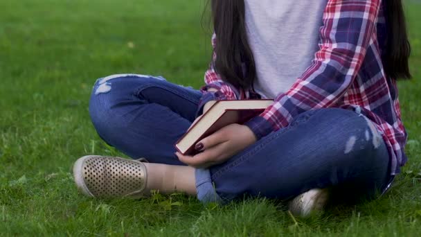 Jonge vrouw zittend op het gras, bedrijf gesloten boek, recreatieve activiteit, ontspannen — Stockvideo