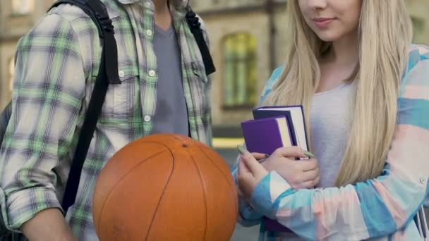 Хлопець з баскетбольним м'ячем розмовляє з дівчиною з книгами, популярний хлопець і ботанік, флірт — стокове відео