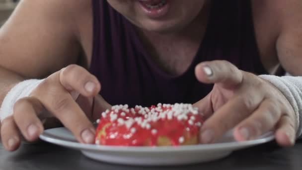 Hombre adulto con sobrepeso tumbado en el suelo y masticando donut con apetito, primer plano — Vídeos de Stock