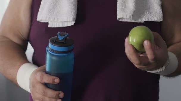 Sovrappeso maschio bere acqua naturale e mangiare mela verde dopo l'allenamento, dieta — Video Stock