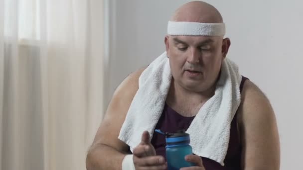 Homme obèse en vêtements de sport assis sur le tapis et l'eau potable après l'entraînement actif — Video