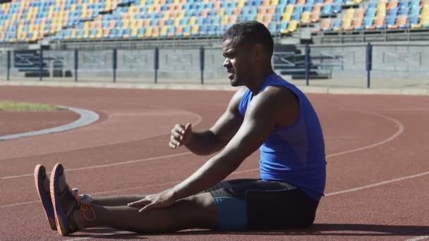 Atleta latino limpiando el sudor de la frente y frotando cansado de las piernas de entrenamiento — Vídeos de Stock