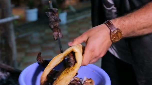 El hombre que quita la carne cocida de los pinchos, va a tratar a los invitados, la hospitalidad — Vídeos de Stock