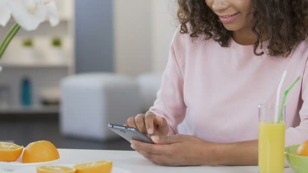 Sonriente chica biracial desplazándose en el teléfono inteligente y utilizando la aplicación de dieta, salud — Vídeos de Stock