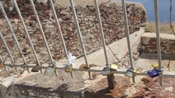 SANTORINI, GREECE - CIRCA JULY 2014: Sightseeing on the island. Iron fence with padlocks hanging on bars at seacoast fortress, symbols of love — Stock Video