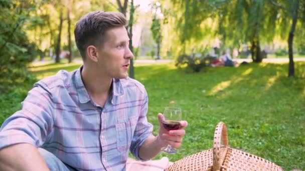 Novio contando historias interesantes a su novia, tratando su vino al aire libre — Vídeo de stock