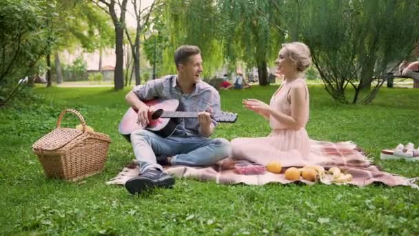 Coppia con appuntamento romantico, cantare canzoni e suonare la chitarra, seduto nel parco — Video Stock