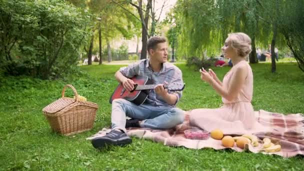 Chica alegre bailando alegremente y cantando a su novio tocando la guitarra, fecha — Vídeo de stock