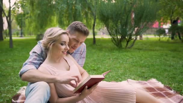 Chico leyendo libro a su novia, pareja disfrutando de ocio en parque juntos — Vídeo de stock