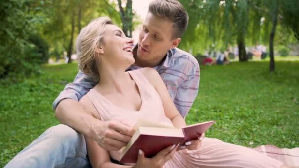 Пара влюбленных, сидящих на ковре, читающих книгу вместе, нежно целующихся в перерывах — стоковое видео