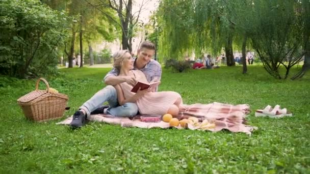 Любящие пары обсуждают книгу плотно сидя на ковре во время пикника, романтическое свидание — стоковое видео