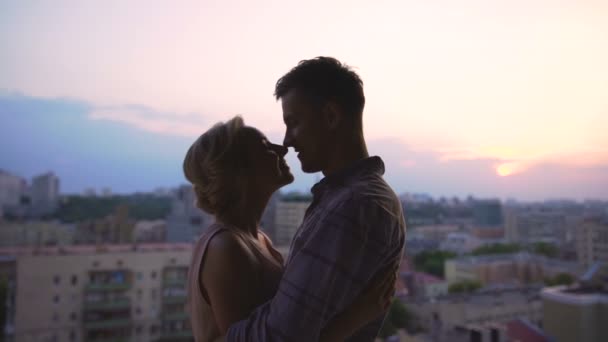 Hermosa pareja disfrutando de abrazos, admirando la puesta de sol desde el techo de un edificio alto — Vídeo de stock