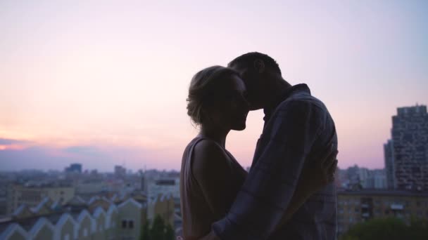 Красивый мужчина нежно целует свою девушку, согревая ее от вечерней прохлады, заката — стоковое видео