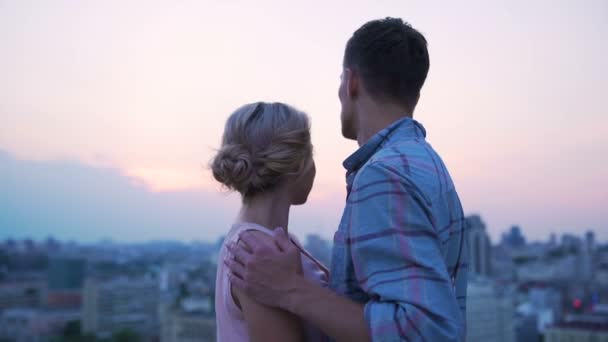 Мужчина в любви гладит плечи своей возлюбленной, любуясь закатом на крыше — стоковое видео